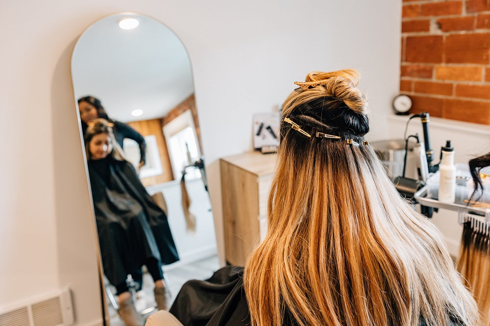 A hair stylist installs hand-tied hair extensions into a woman's hair in a luxury spa setting