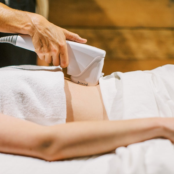 A medspa esthetician uses a HIFU wand to direct ultrasound energy into a spa guests abdomen to stimulate collagen production and tighten the skin.
