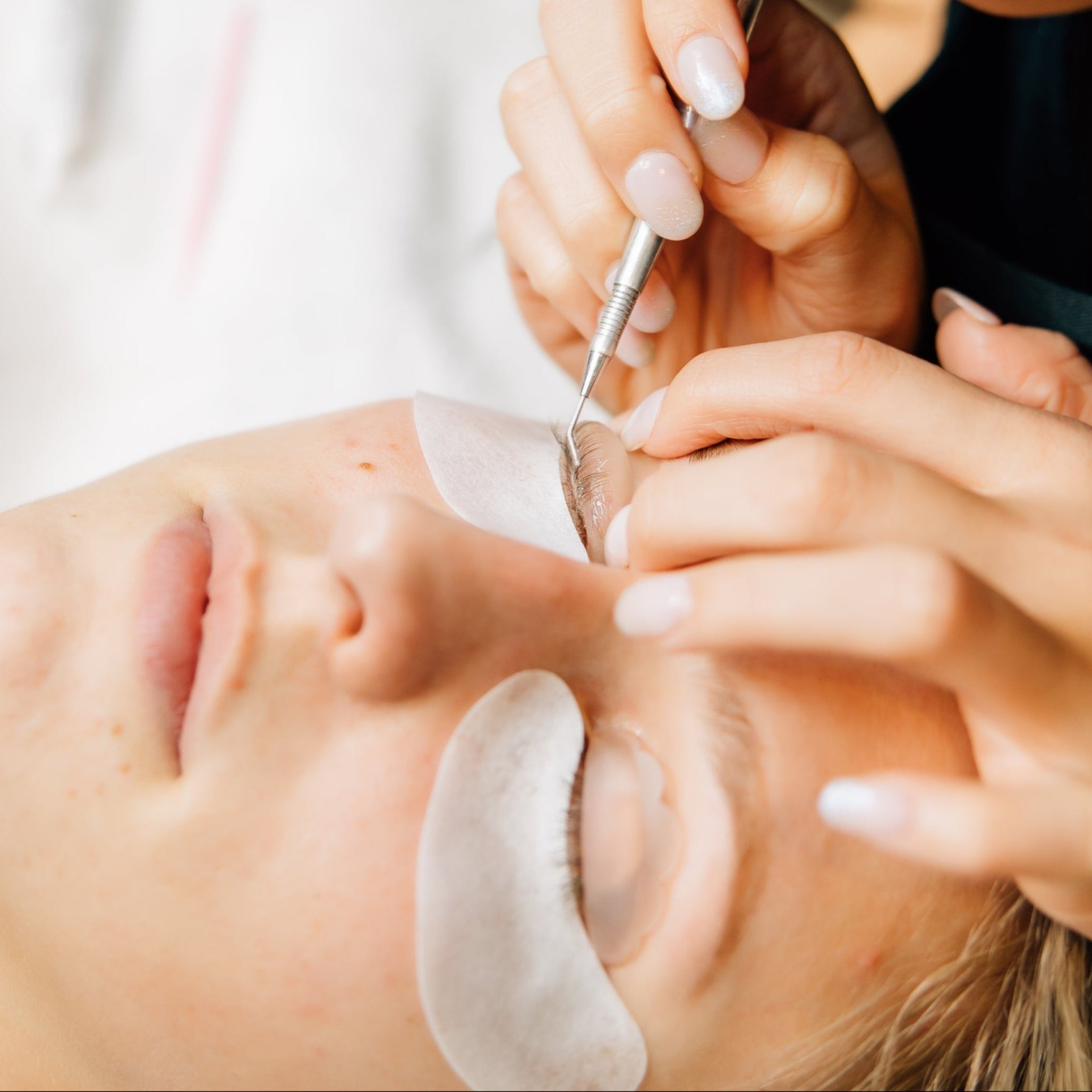 A woman relaxes with her eyes closed while receiving a lash lift service in a luxury spa.