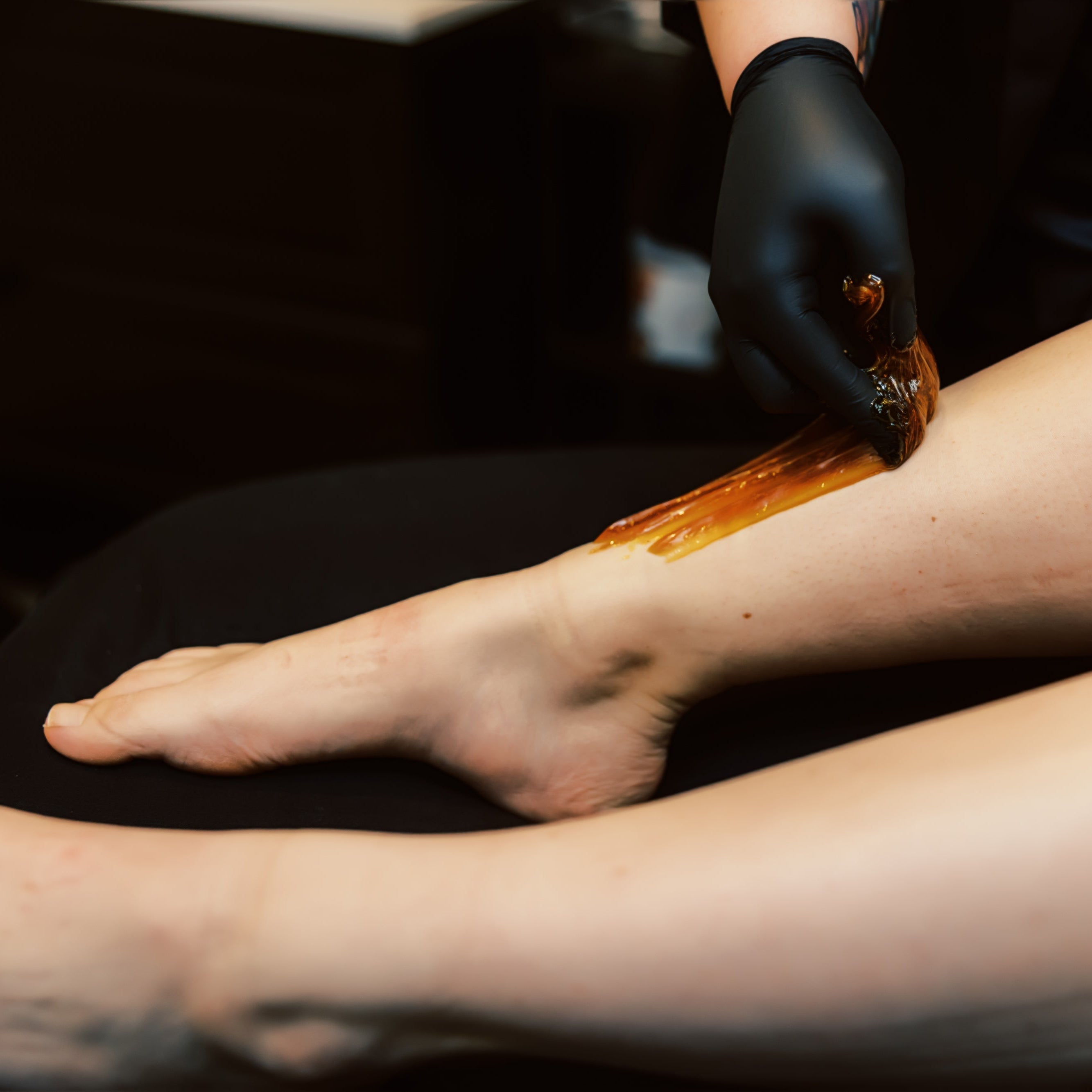 A close-up of a leg undergoing hair removal using a sugaring technique