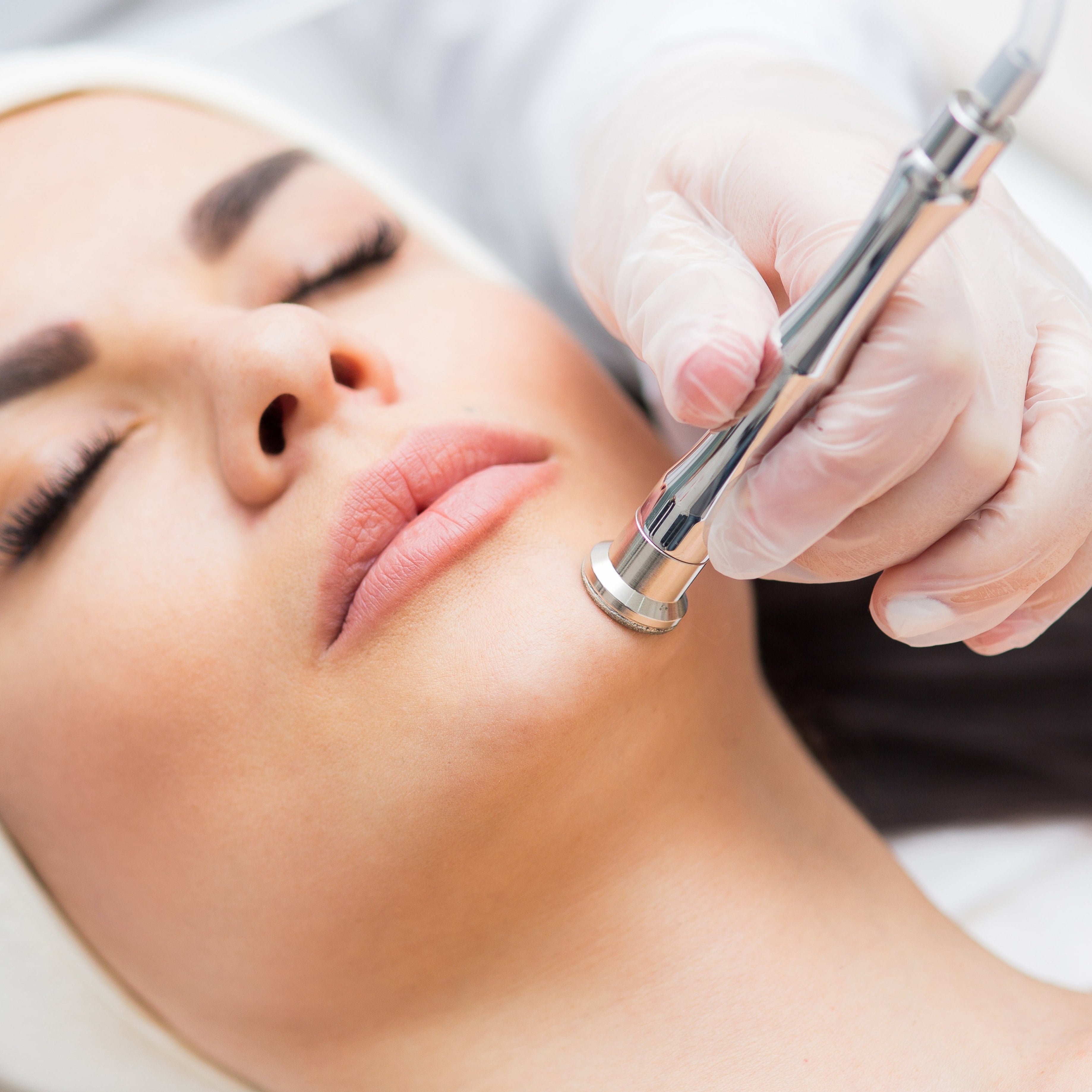 A woman closes her eyes during a microdermabrasion facial in a luxury spa setting