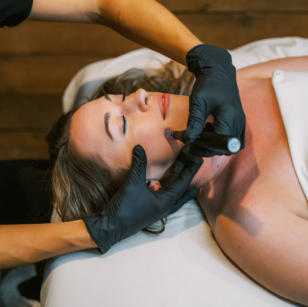 A woman relaxes with her eyes closed while receiving a microneedling treatment in a luxury spa setting.