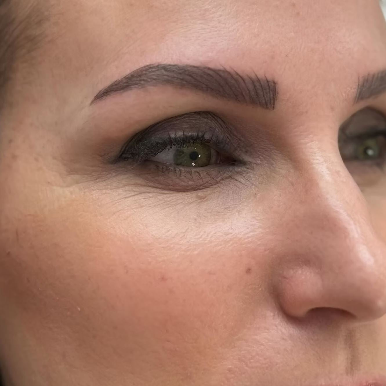 A close-up image of a woman's eye shows impactful results of a semi-permanent makeup treatment for powder brows