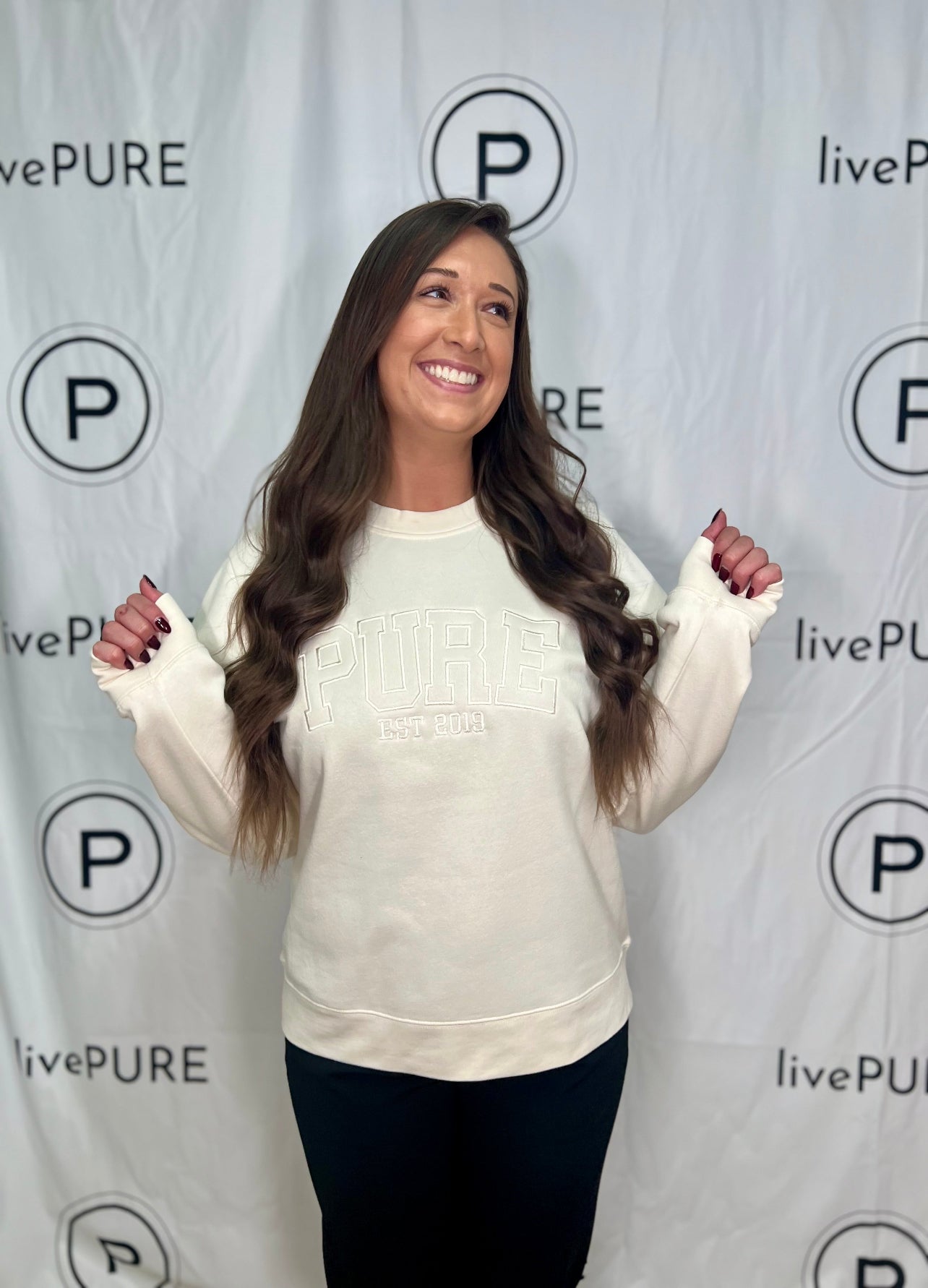 Woman wearing a beige sweatshirt with 'livePURE' branding against a branded backdrop.