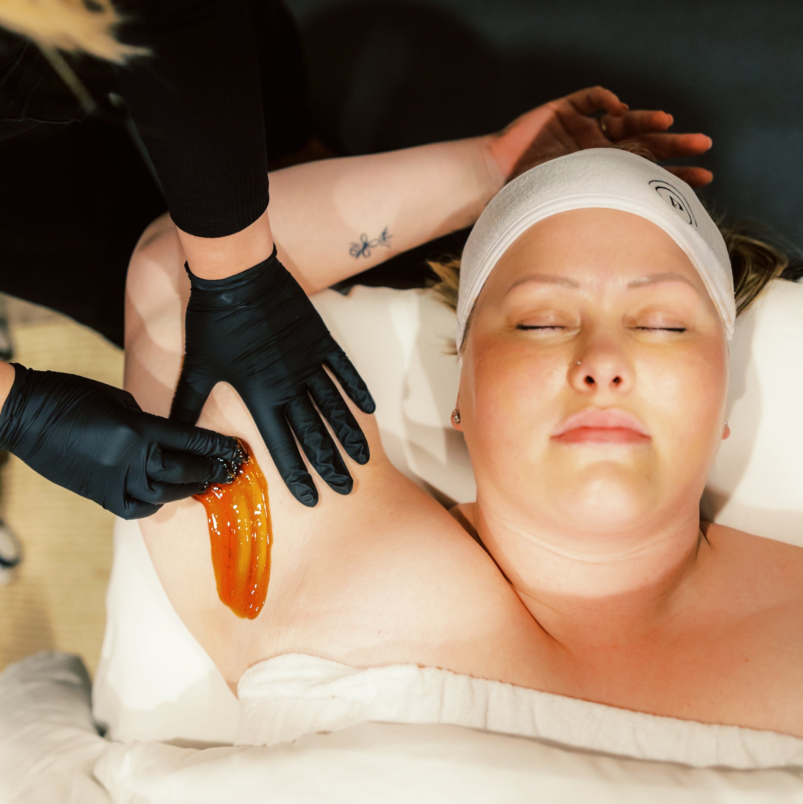 A woman relaxes with her eyes closed while receiving an underarm sugaring treatment for hair removal in a luxury spa setting