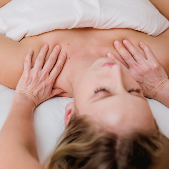 A woman relaxes with her eyes closed while receiving a therapeutic massage focused on muscles in the upper body.