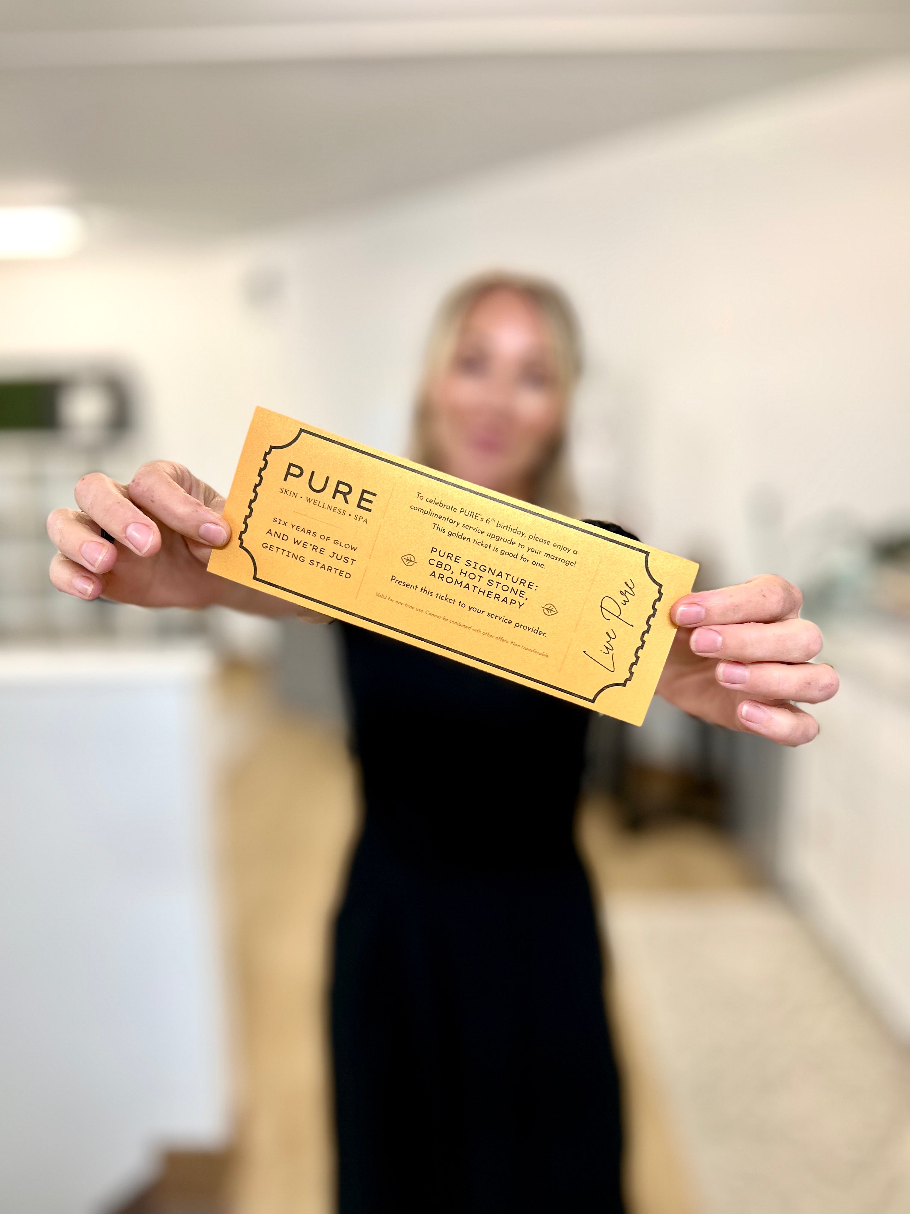 Woman holds a golden ticket showing she won a service upgrade at luxury spa Pure Skin Wellness Spa. 