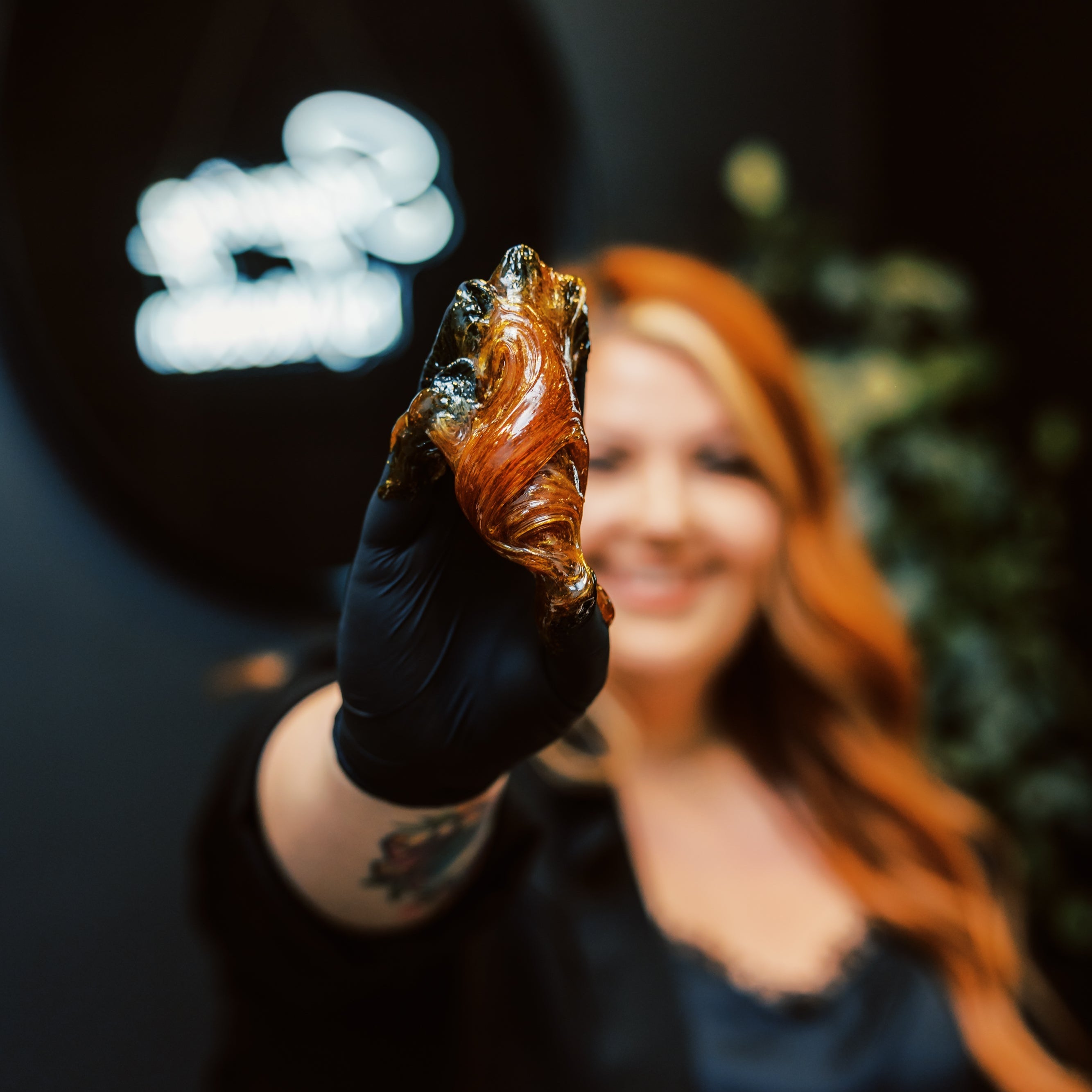 A female esthetician extends a gloved hand holding sugaring paste in a luxury spa setting