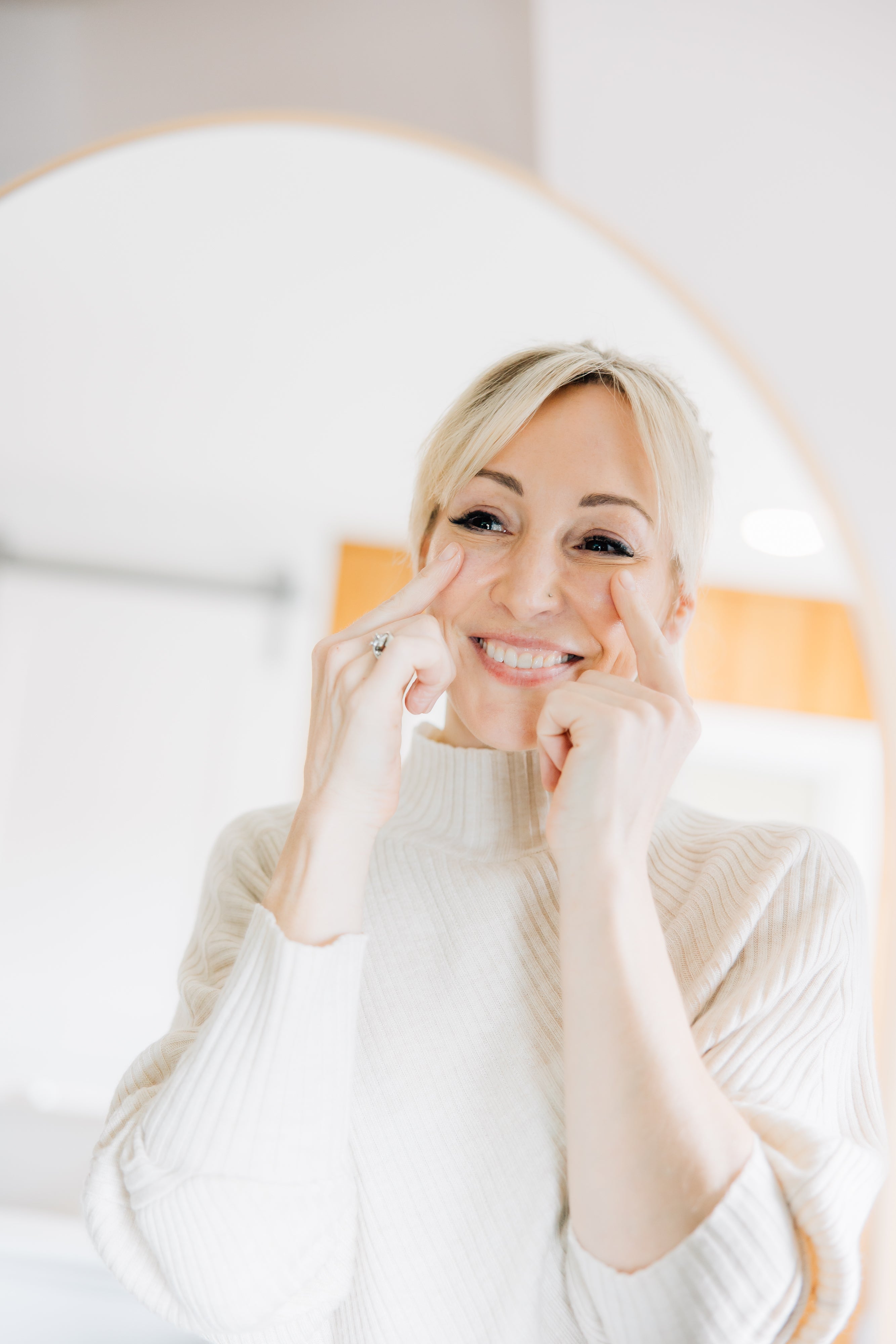 Woman smiling in the mirror while applying professional skincare products during her daily routine